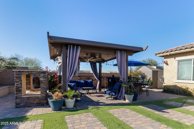 view of patio featuring ceiling fan, a gazebo, and an outdoor living space with a fireplace