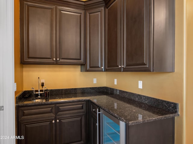 kitchen featuring dark brown cabinetry, beverage cooler, and dark stone countertops