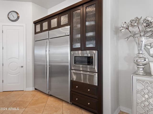 kitchen featuring dark brown cabinetry, built in appliances, and light tile patterned floors