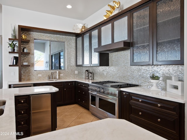 kitchen with sink, backsplash, dark brown cabinetry, light tile patterned flooring, and range with two ovens