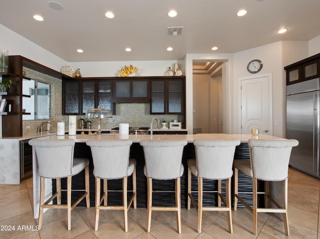 kitchen with tasteful backsplash, an island with sink, stainless steel built in refrigerator, and a kitchen breakfast bar