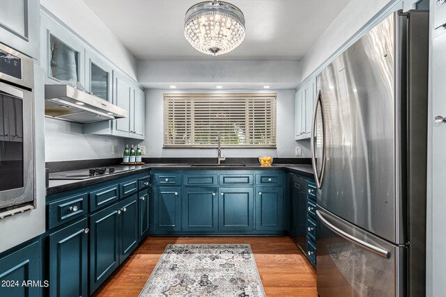 kitchen with sink, light wood-type flooring, stainless steel appliances, blue cabinetry, and an inviting chandelier