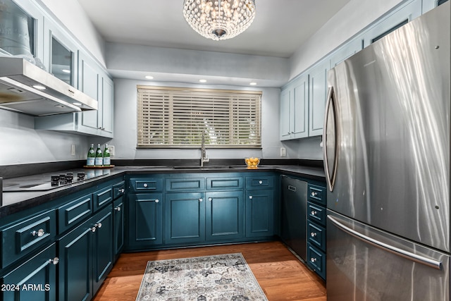 kitchen with wall chimney range hood, light wood-type flooring, stainless steel appliances, sink, and blue cabinets