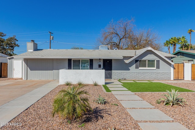 ranch-style home featuring concrete driveway, a shingled roof, and fence