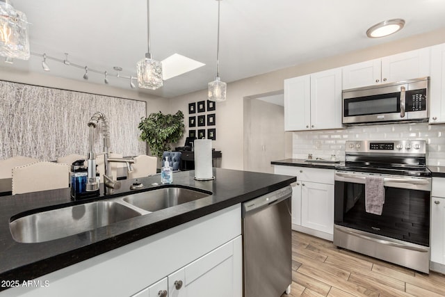 kitchen with decorative backsplash, dark countertops, appliances with stainless steel finishes, light wood-style floors, and a sink