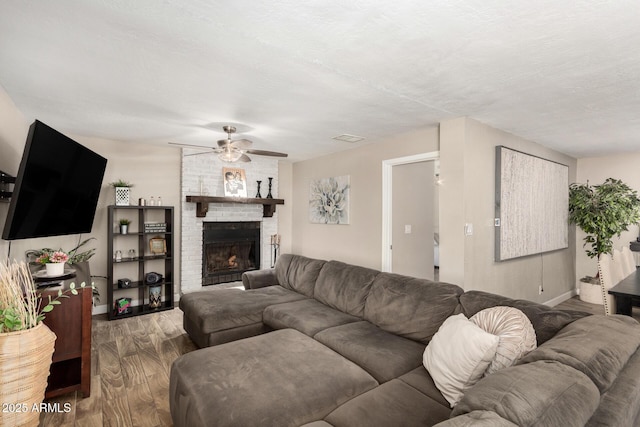 living room with ceiling fan, a fireplace, wood finished floors, visible vents, and baseboards