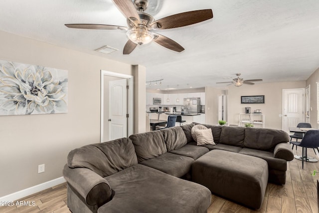 living area with visible vents, light wood-style flooring, a ceiling fan, a textured ceiling, and baseboards