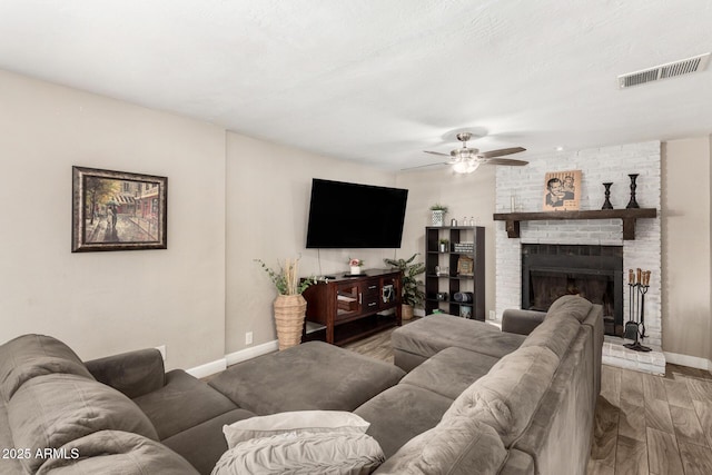 living area featuring baseboards, visible vents, ceiling fan, wood finished floors, and a brick fireplace