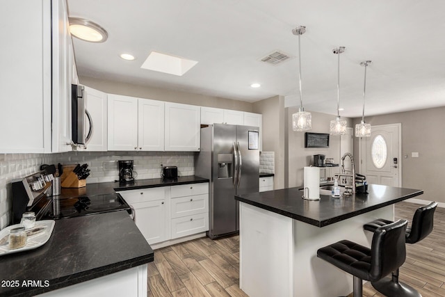 kitchen featuring tasteful backsplash, visible vents, a kitchen breakfast bar, stainless steel appliances, and light wood-style floors