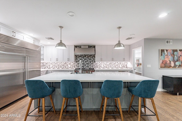 kitchen featuring a spacious island, pendant lighting, white cabinets, wall chimney range hood, and stainless steel appliances