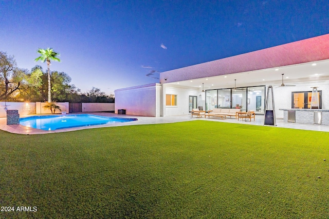 pool at dusk with ceiling fan, outdoor lounge area, a lawn, and a patio