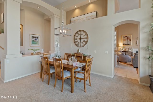 dining room featuring a towering ceiling, an inviting chandelier, decorative columns, and carpet floors