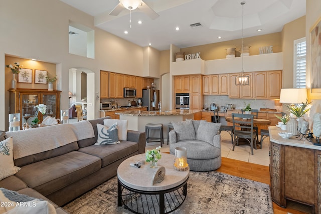 living room with a towering ceiling, a tray ceiling, ceiling fan, and light hardwood / wood-style flooring