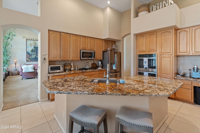 kitchen with stone counters, light tile patterned floors, stainless steel appliances, an island with sink, and sink