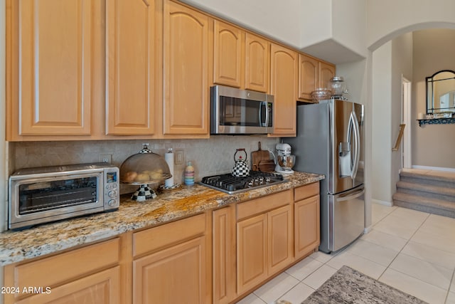 kitchen featuring tasteful backsplash, light tile patterned floors, light brown cabinetry, light stone counters, and appliances with stainless steel finishes