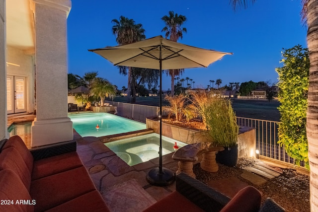 pool at night featuring a patio area and an in ground hot tub