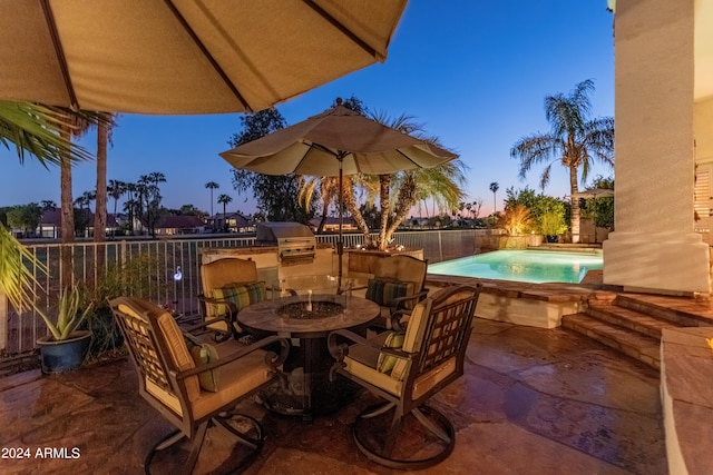 patio terrace at dusk featuring area for grilling and a fenced in pool