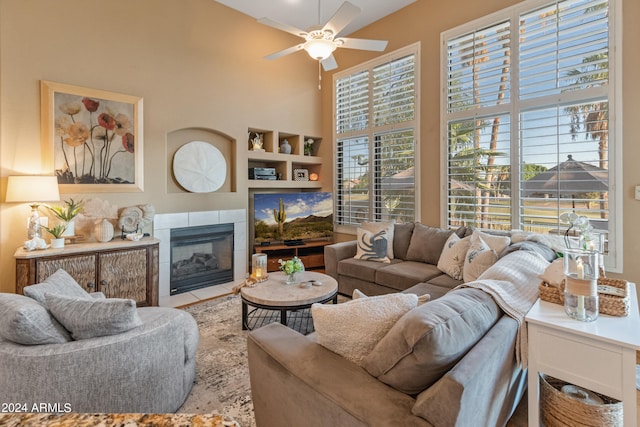 living room featuring ceiling fan, a towering ceiling, and a tile fireplace