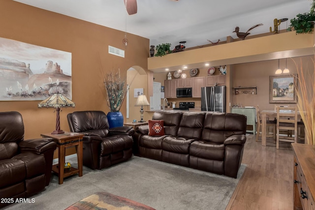 living room featuring light wood-style flooring, arched walkways, ceiling fan, and visible vents