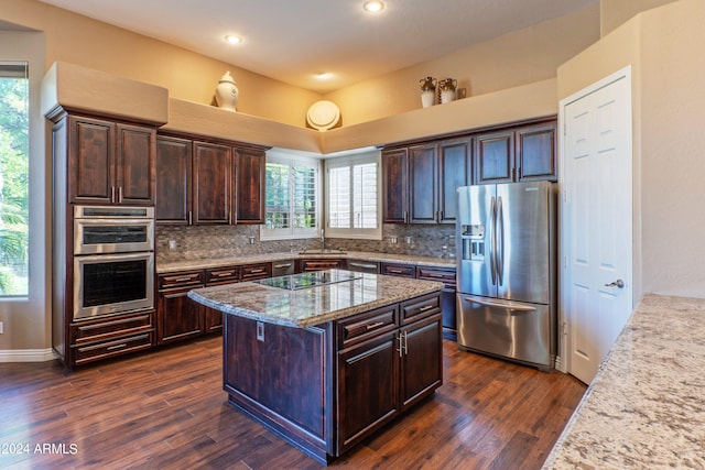 kitchen with appliances with stainless steel finishes, light stone counters, dark brown cabinets, sink, and a kitchen island