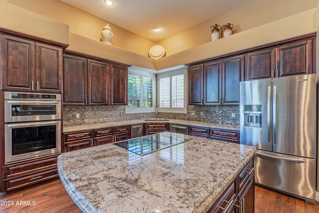 kitchen featuring a center island, backsplash, light stone counters, dark brown cabinetry, and stainless steel appliances