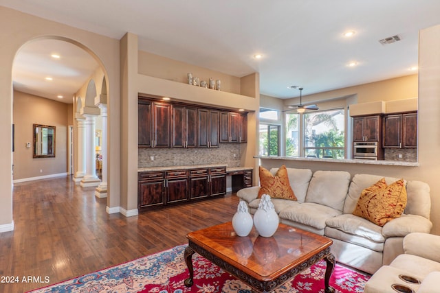 living room with decorative columns, ceiling fan, and dark wood-type flooring