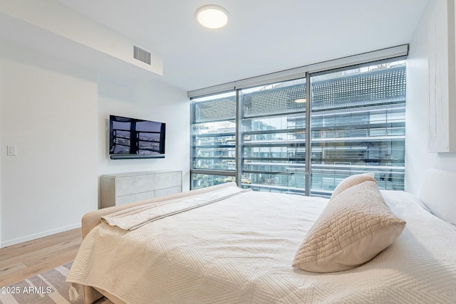 bedroom featuring visible vents, wood finished floors, baseboards, and expansive windows