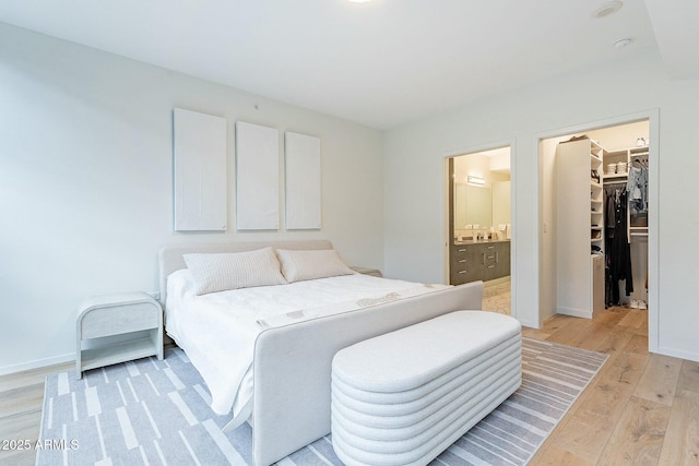 bedroom with baseboards, a spacious closet, light wood-style floors, a closet, and connected bathroom