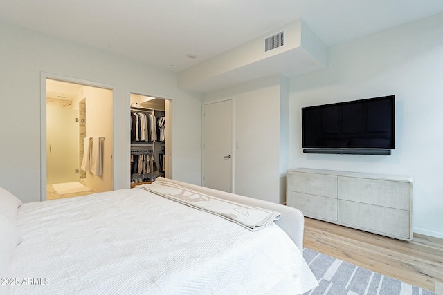 bedroom featuring wood finished floors, visible vents, a closet, a walk in closet, and connected bathroom