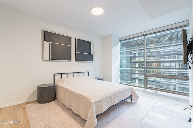 bedroom with expansive windows, baseboards, and wood finished floors