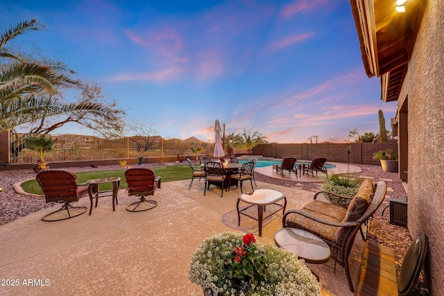 patio terrace at dusk featuring a fenced in pool