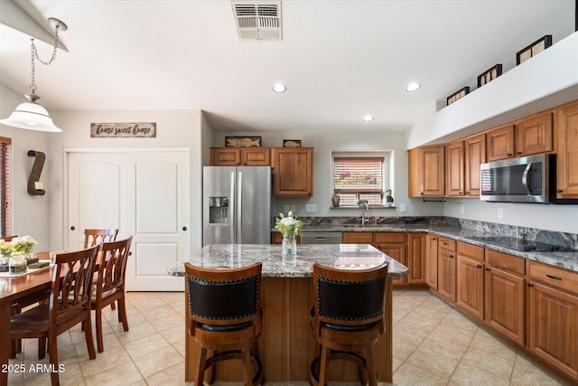 kitchen with brown cabinetry, visible vents, a sink, appliances with stainless steel finishes, and a kitchen breakfast bar