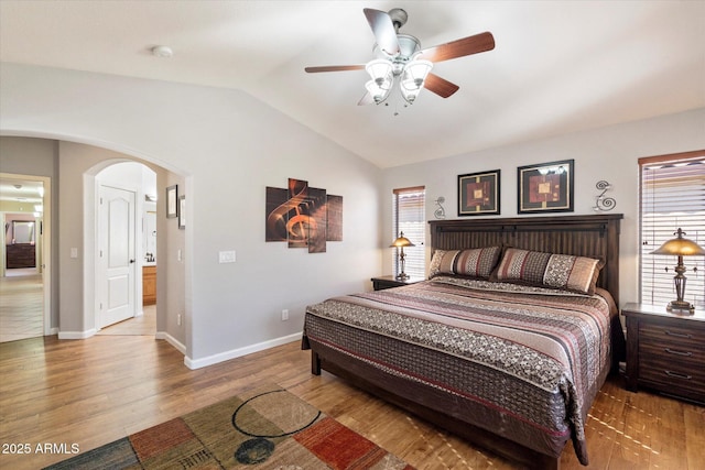 bedroom featuring a ceiling fan, wood finished floors, baseboards, arched walkways, and vaulted ceiling