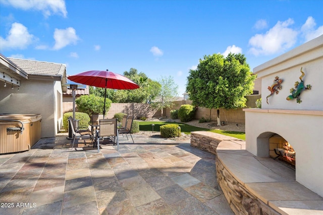 view of patio with a fenced backyard, a hot tub, outdoor dining area, and a lit fireplace