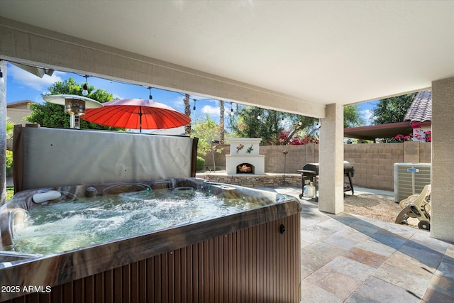 view of patio with cooling unit, fence, area for grilling, a warm lit fireplace, and a hot tub