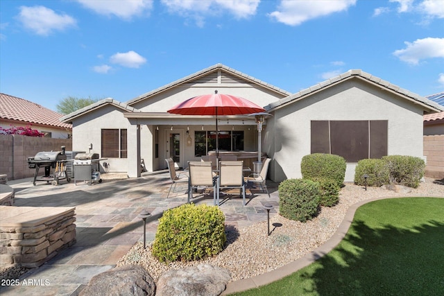 rear view of property featuring outdoor dining area, fence, and stucco siding