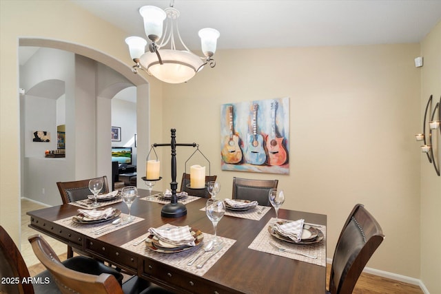 dining space with wood finished floors, baseboards, arched walkways, and a chandelier