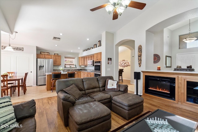 living area with visible vents, recessed lighting, arched walkways, light wood-style floors, and lofted ceiling