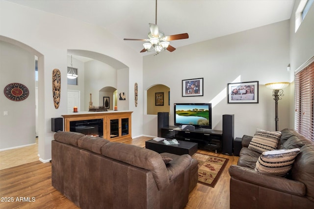 living area featuring high vaulted ceiling, light wood-type flooring, baseboards, and a ceiling fan