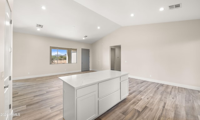 kitchen featuring lofted ceiling, light stone counters, white cabinetry, light hardwood / wood-style floors, and a center island