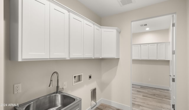 clothes washing area with electric dryer hookup, hookup for a washing machine, sink, light wood-type flooring, and cabinets