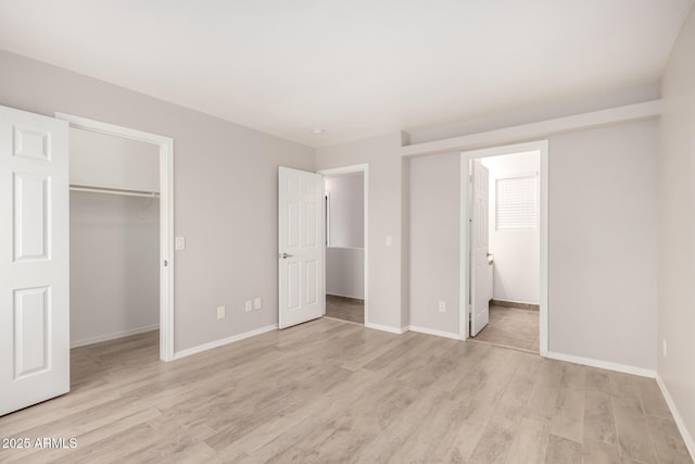 unfurnished bedroom featuring connected bathroom, a spacious closet, a closet, and light wood-type flooring