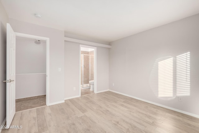 unfurnished bedroom with ensuite bath and light wood-type flooring