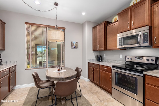 kitchen with decorative light fixtures, light stone counters, light tile patterned floors, and stainless steel appliances