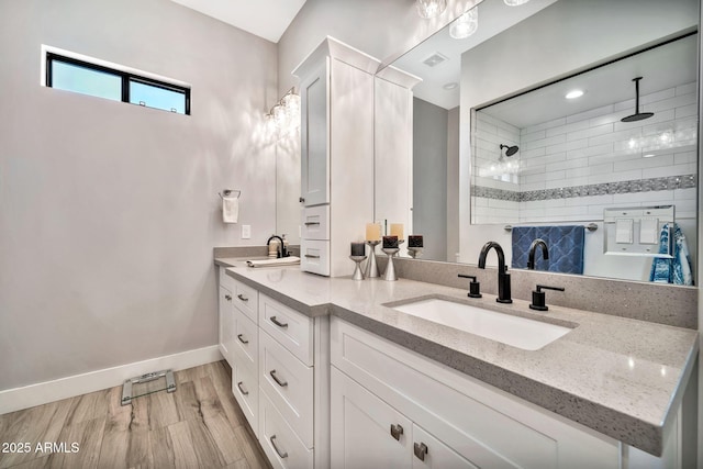 bathroom with double vanity, a sink, wood finished floors, tiled shower, and baseboards