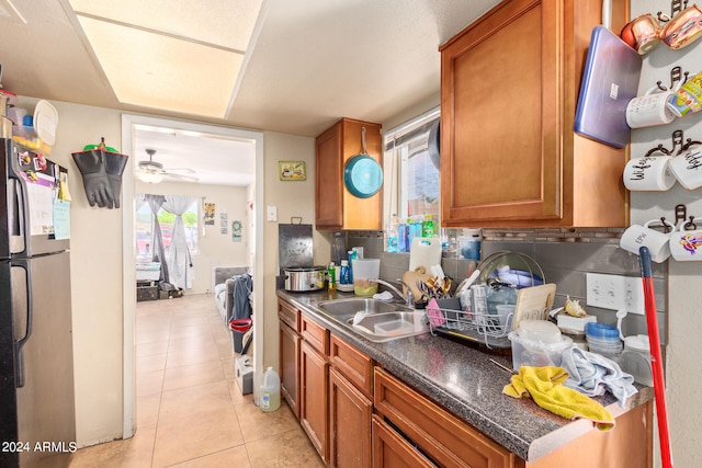 kitchen featuring ceiling fan, tasteful backsplash, light tile flooring, sink, and stainless steel refrigerator