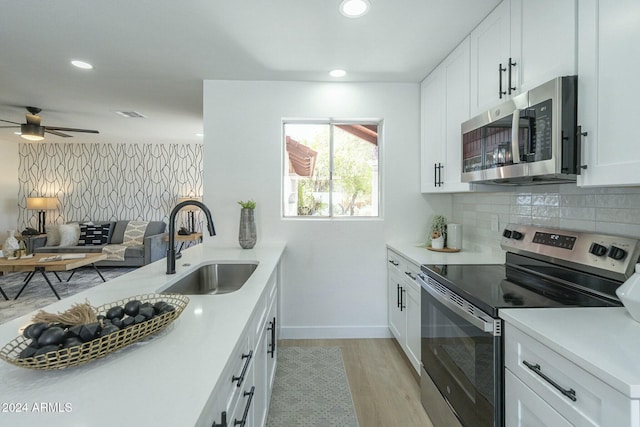 kitchen with sink, light wood-type flooring, tasteful backsplash, white cabinetry, and stainless steel appliances