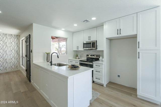 kitchen with tasteful backsplash, stainless steel appliances, sink, light hardwood / wood-style flooring, and white cabinetry