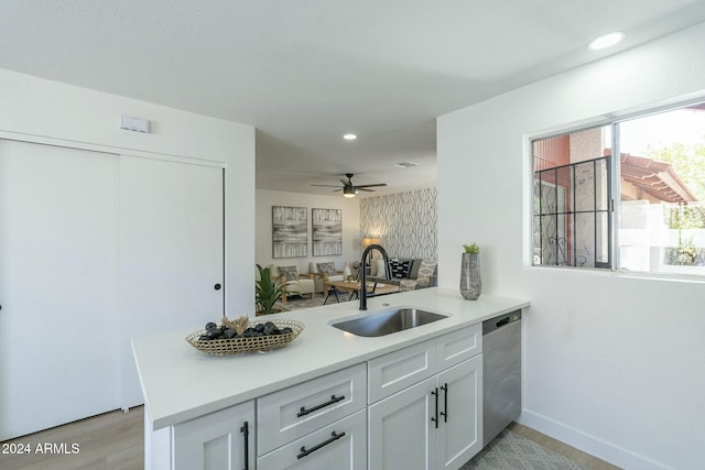 kitchen featuring kitchen peninsula, stainless steel dishwasher, sink, light hardwood / wood-style flooring, and white cabinetry