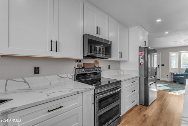 kitchen featuring appliances with stainless steel finishes, white cabinetry, light stone countertops, and light wood-type flooring